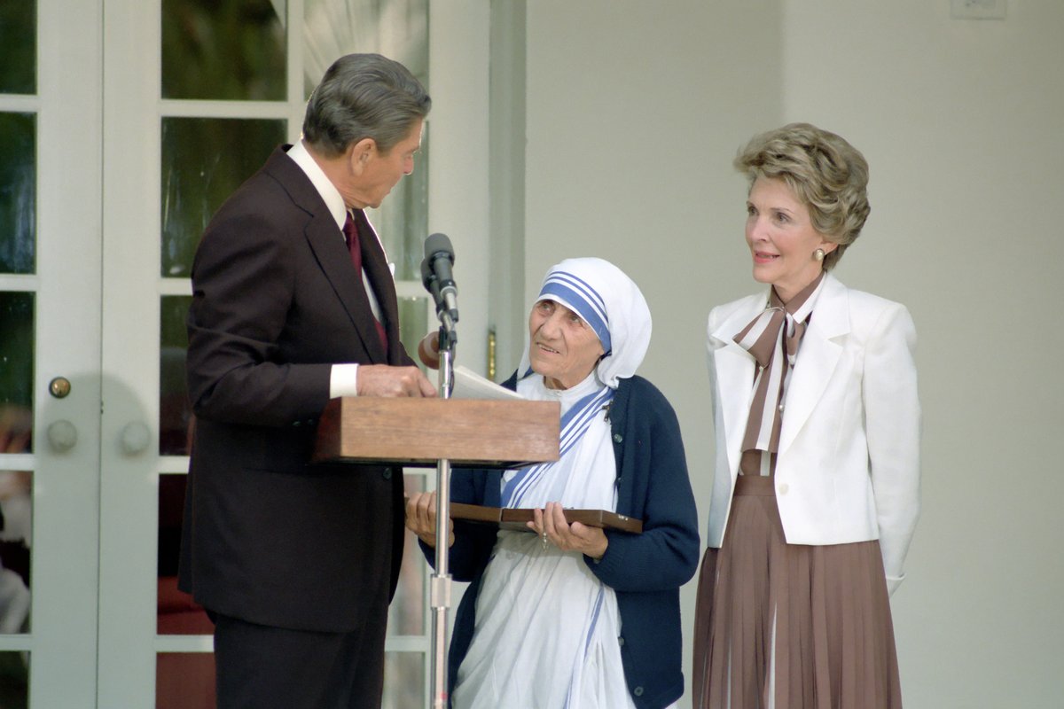 An elderly nun in a white and blue habit stands at a podium beside President Ronald Reagan, who presents her with an award, as First Lady Nancy Reagan looks on.